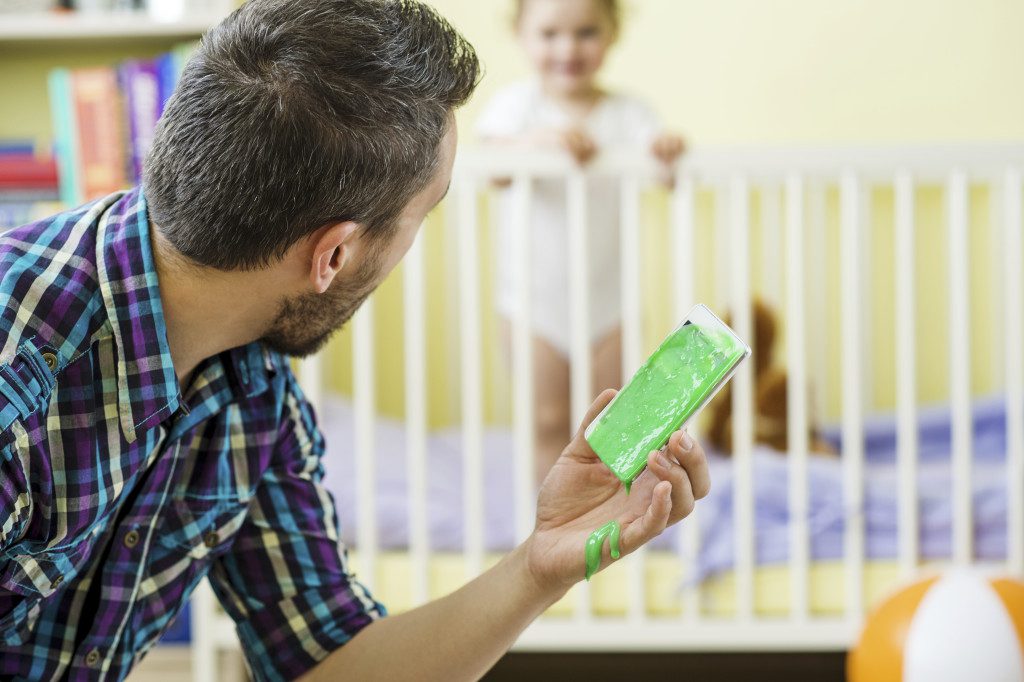 Father holding damaged smart phone and his little daughter in background